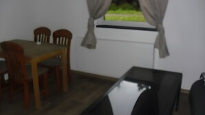 A dining area with a table and chairs, a window with curtains, and a black chair in the foreground. - Apartment 'Gramelower See 1' with Shared Garden (Teschendorf)