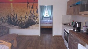 A compact kitchen with a bed, a dining area, and a mural of tall grasses. - Apartment 'Gramelower See 1' with Shared Garden (Teschendorf)