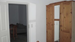 A room with a white door, a wooden wardrobe, a grey sofa, and a wooden chair. - Apartment 'Gramelower See 1' with Shared Garden (Teschendorf)
