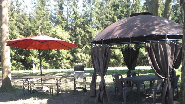 A covered picnic area with tables and chairs, a grill, and an umbrella. - Apartment 'Gramelower See 1' with Shared Garden (Teschendorf)
