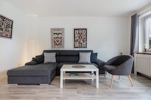 A modern living room with a sectional sofa, a round coffee table, and a grey armchair. - Holiday Home 'Ferienhaus Heide' with Private Terrace and Wi-Fi (Bad Fallingbostel)