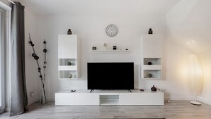 A modern living room with a flat-screen TV, white shelving, a clock, and a floor lamp.