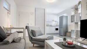 Un salon moderne avec un canapé gris, une table basse, un téléviseur et une cuisine en arrière-plan.