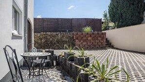 Une terrasse avec une table et des chaises, un mur en pierre et un grand arbre.