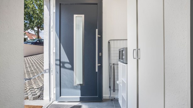 Un hall d’entrée moderne avec une porte sombre, une poignée en métal et un panneau de verre.
