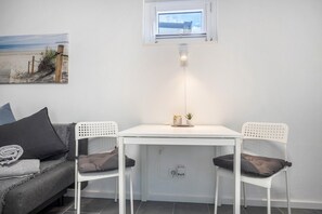 A small room with a white table, two chairs, a grey sofa, a painting, and a window. - Studio Apartment 'Ferienwohnung Heide 2' with Private Terrace and Wi-Fi (Walsrode)