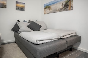 Una cama con ropa de cama gris, un cabecero gris y una pared blanca con tres cuadros enmarcados.