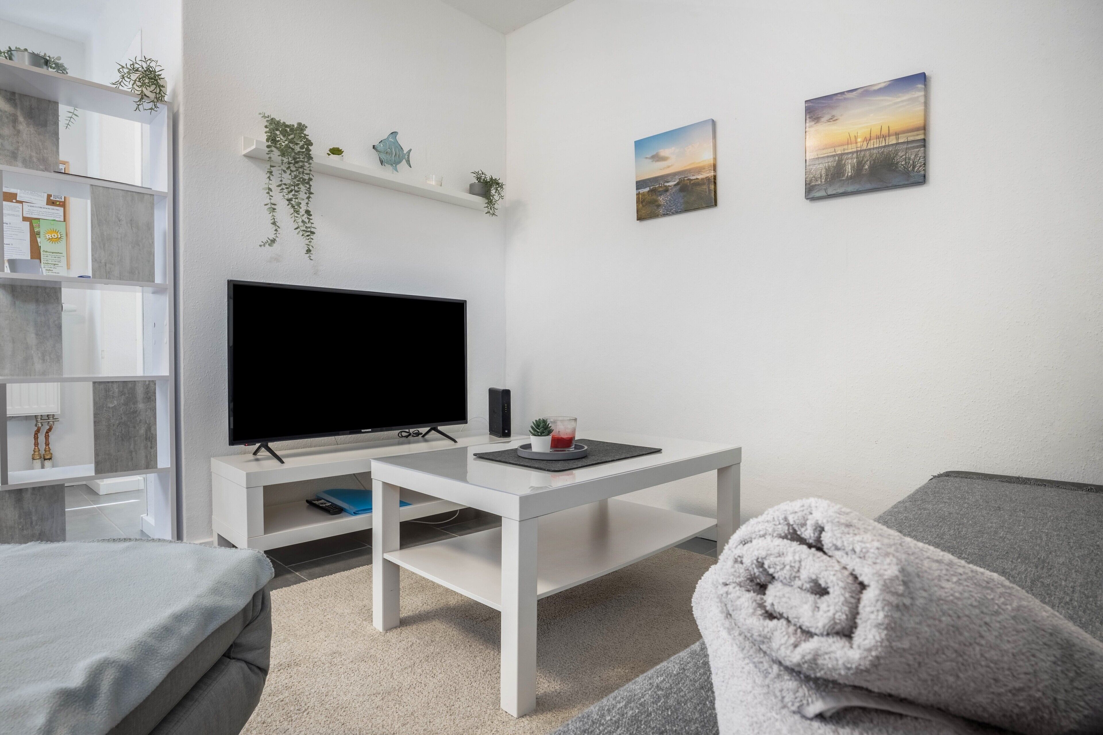 Ein modernes Wohnzimmer mit Flachbildfernseher, weißen Möbeln und Zimmerpflanzen.