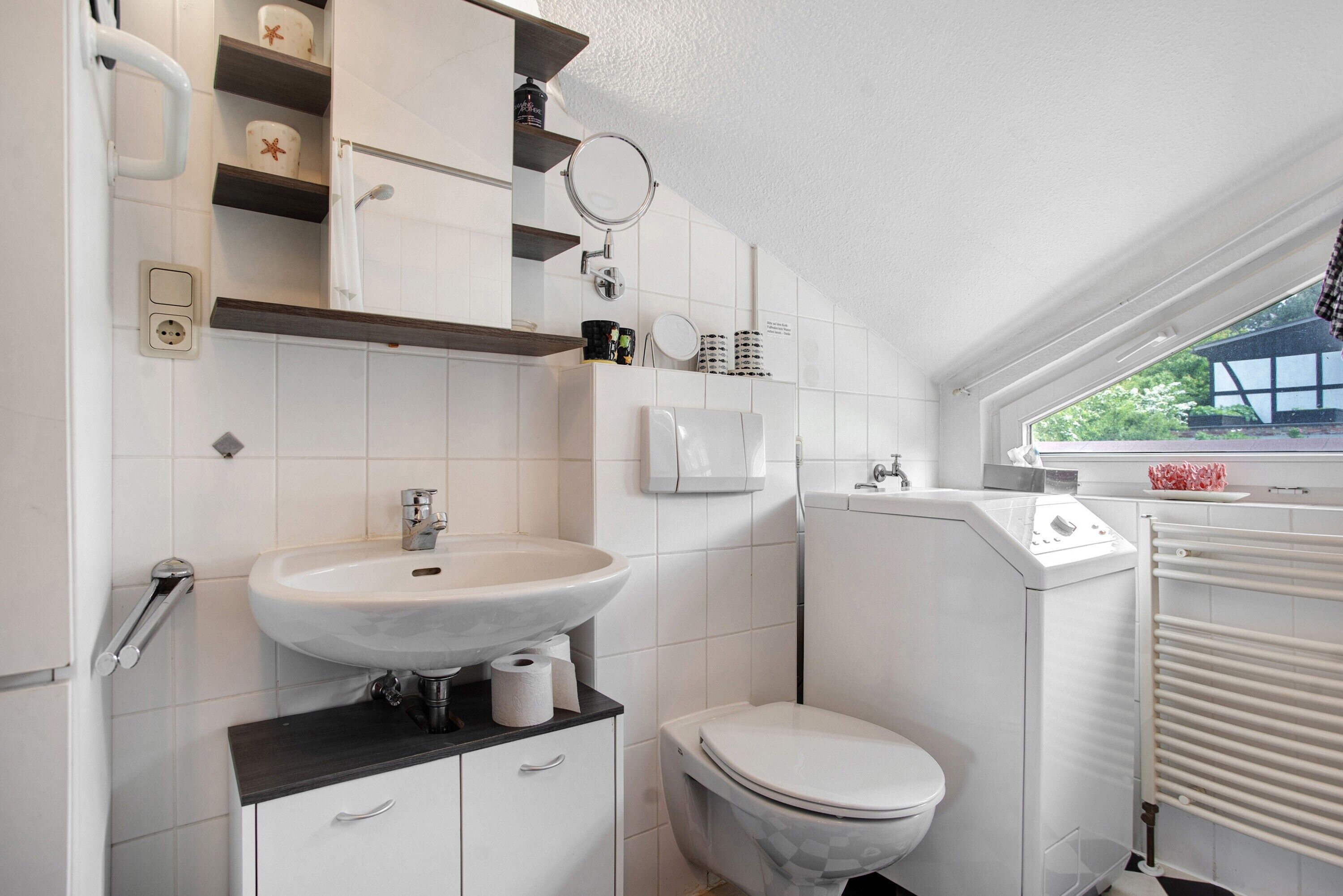 Et badeværelse med en hvid vask, toilet og et vindue med udsigt.