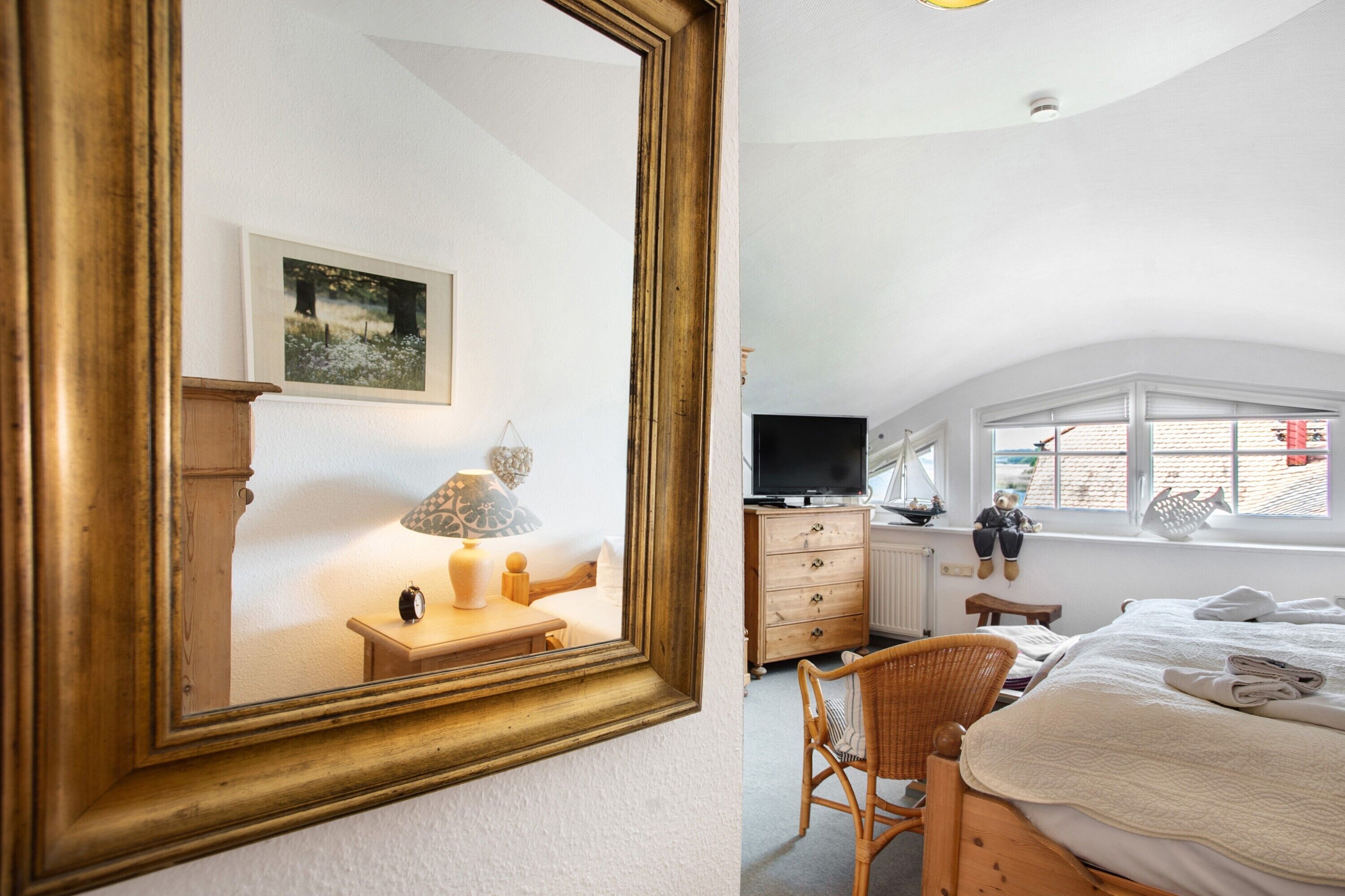 A bedroom with a large mirror, a television, a dresser, a chair, and a bed with a quilt.