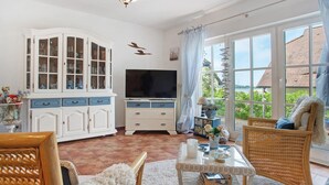 A living room with a television, white cabinets, wicker furniture, and large windows. - Apartment 'Fewo Yachthafenblick Nr 5' with Sea View, Private Terrace and Wi-Fi (Ostseebad Sellin)