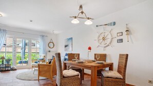 A dining area with wicker chairs, a wooden table, and a ship's wheel decoration on the wall. - Apartment 'Fewo Yachthafenblick Nr 5' with Sea View, Private Terrace and Wi-Fi (Ostseebad Sellin)