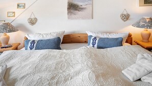 A neatly made bed with a white and blue patterned bedspread, two matching pillows, a wooden headboard, and a wall-mounted picture of a beach scene. - Apartment 'Fewo Yachthafenblick Nr 5' with Sea View, Private Terrace and Wi-Fi (Ostseebad Sellin)