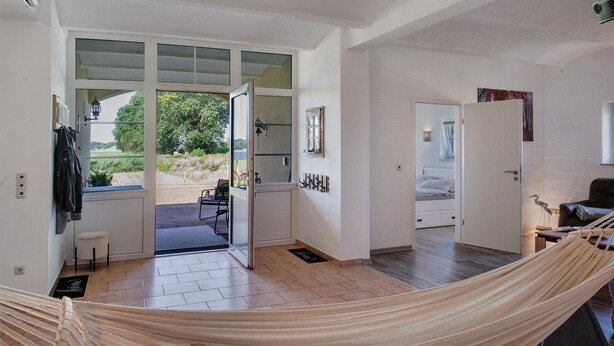 Un intérieur moderne avec un hamac, une porte donnant sur un balcon et une vue sur la verdure environnante.