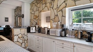 Une cuisine avec un mur en pierre, une machine à café, un mixeur et une fenêtre donnant sur les arbres.