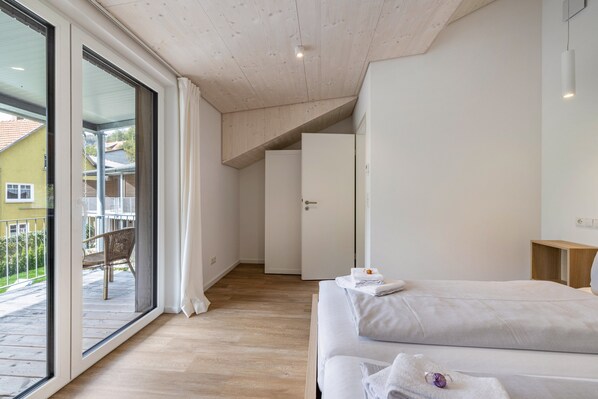 Ein Schlafzimmer mit einer großen Glasschiebetür, die zu einem Balkon führt, einem Bett mit weißer Bettwäsche und einer Holzbalkendecke.