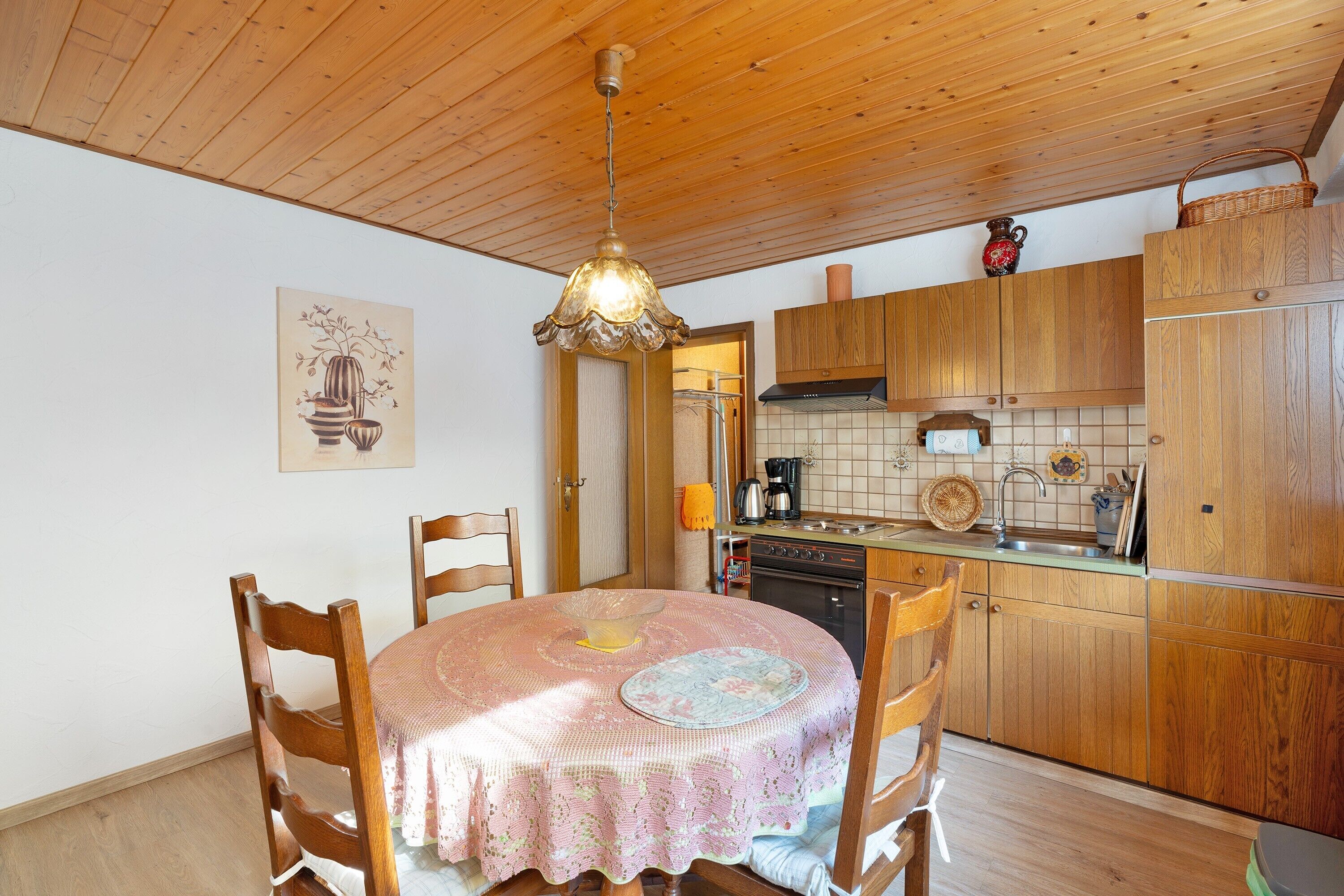 A kitchen with wooden cabinets, a dining table with chairs, a hanging light fixture, and a tiled backsplash.