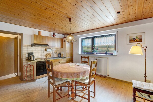 Une cuisine avec des meubles de rangement en bois, une cuisinière, une table à manger avec des chaises, un luminaire suspendu et une fenêtre donnant sur un beau paysage.