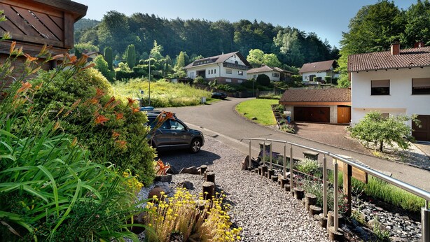 Et boligområde med huse, en grusindkørsel og en bil parkeret på gaden.