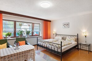 Une chambre à coucher avec un lit, une table de chevet, une lampe, une fenêtre avec des rideaux et une vue sur l’extérieur.