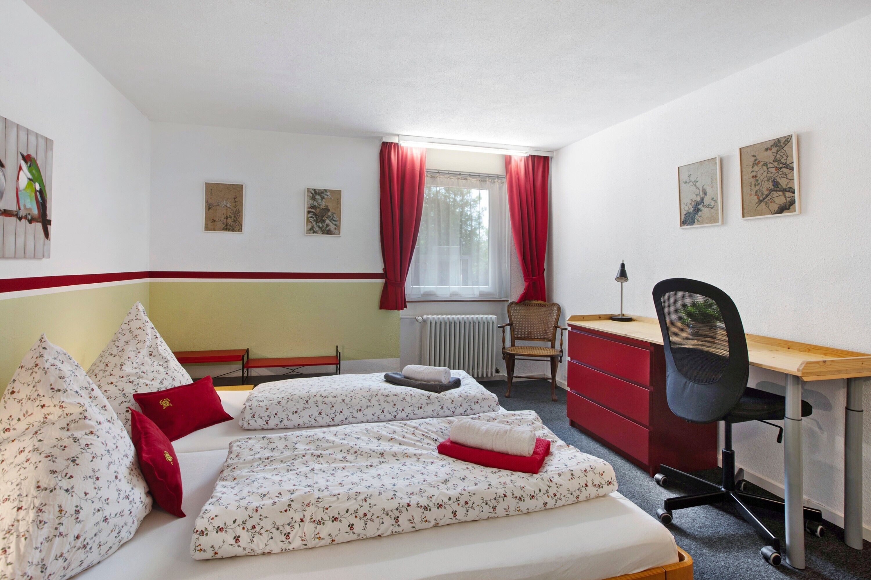 Ein Schlafzimmer mit zwei Betten, einem Schreibtisch, einem Stuhl und Bildern an den Wänden.
