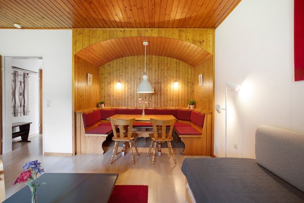 A wooden interior with a dining table, chairs, and a sofa.