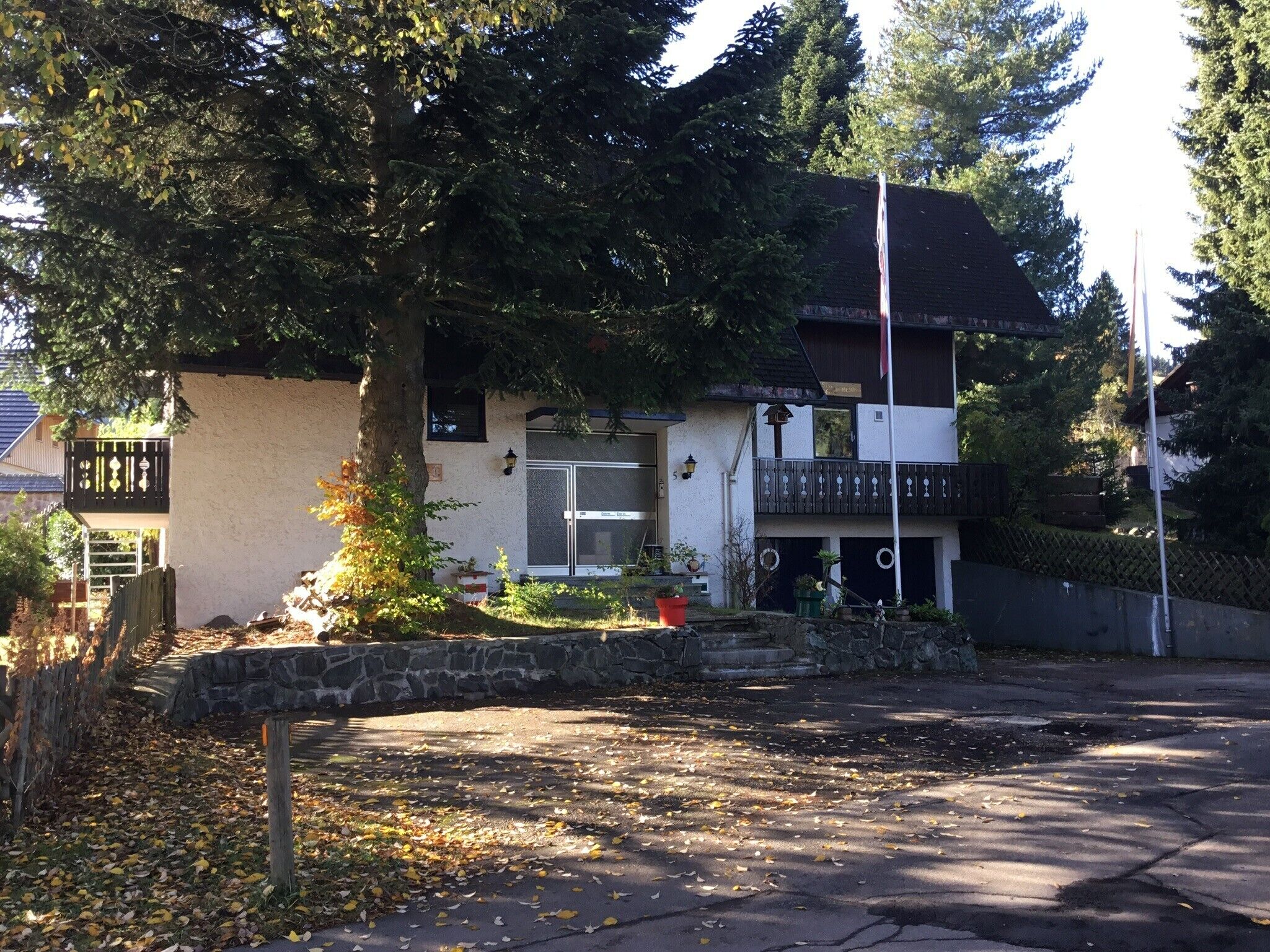 A two-story building with a balcony, a stone wall, and a tree in front.