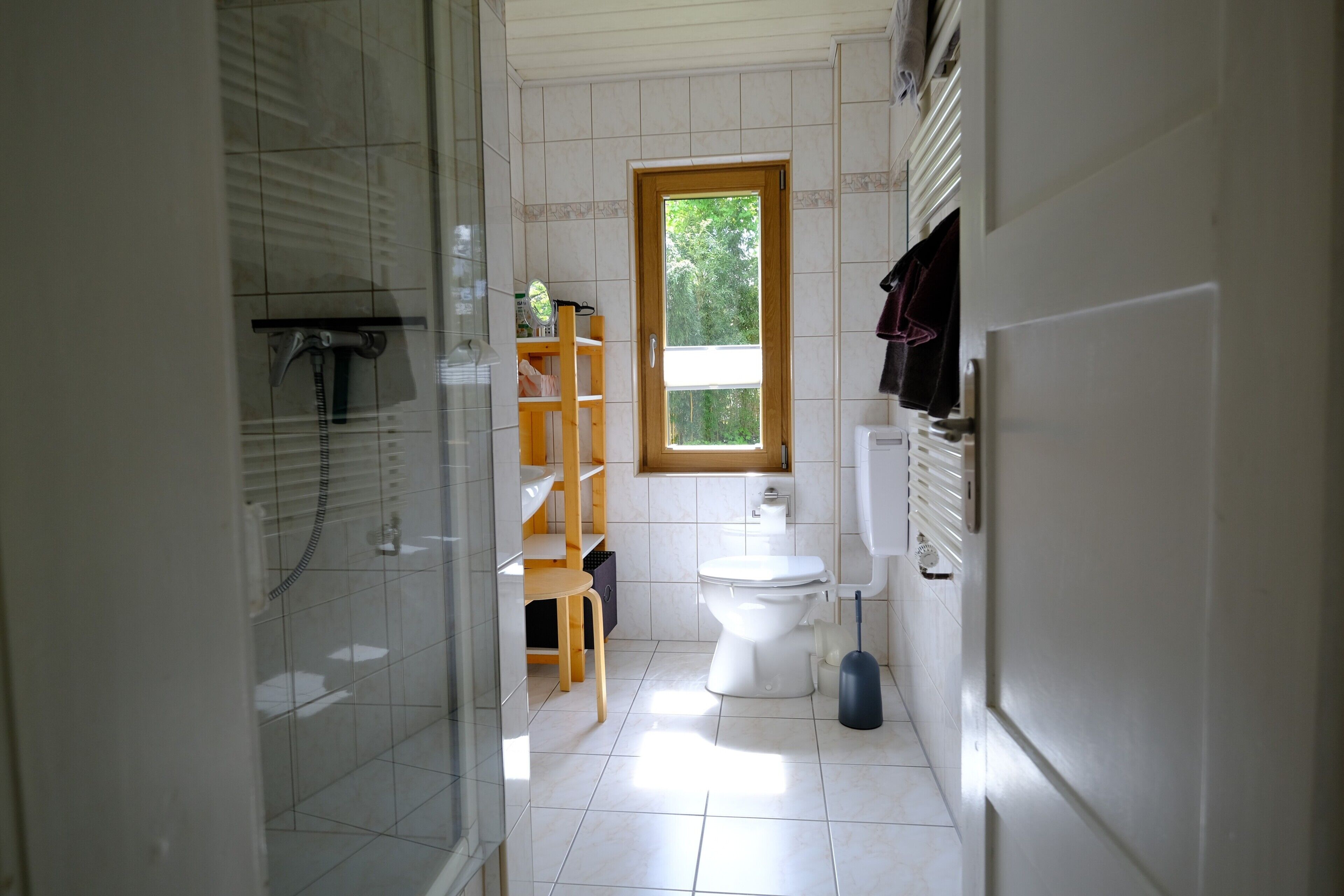 Une salle de bain avec des toilettes, une douche, une fenêtre et une chaise en bois.