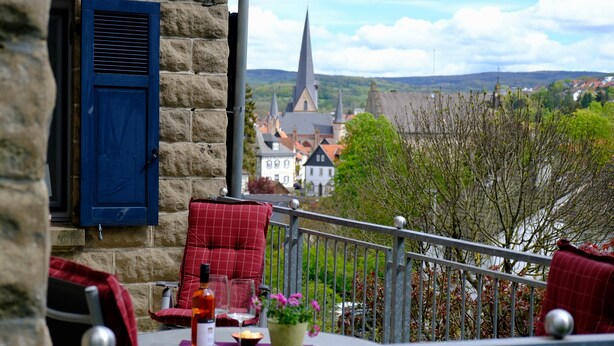 A balcony with a table, chairs, and a view of a church and landscape. - Apartment 'altes forsthaus schotten' with Shared Garden, Balcony and Wi-Fi (Schotten)