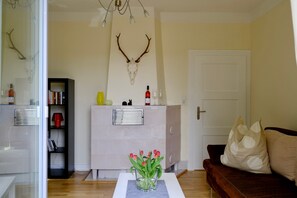 Ein Wohnzimmer mit Kamin, Bücherregal, Couchtisch mit Blumen und einer Couch mit Kissen.