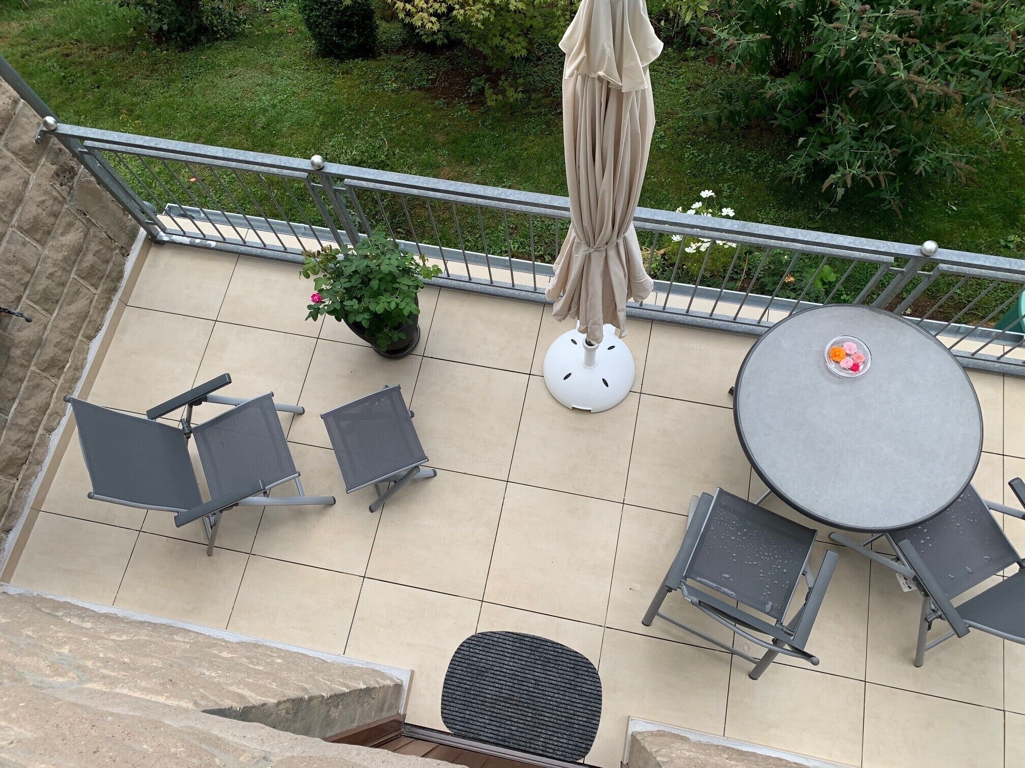 Un balcon avec une table ronde, deux chaises, un pot de fleurs et une rambarde en métal.