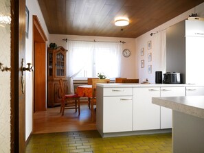 Une cuisine avec des meubles blancs, un plafond en bois, une horloge et une fenêtre avec des rideaux.