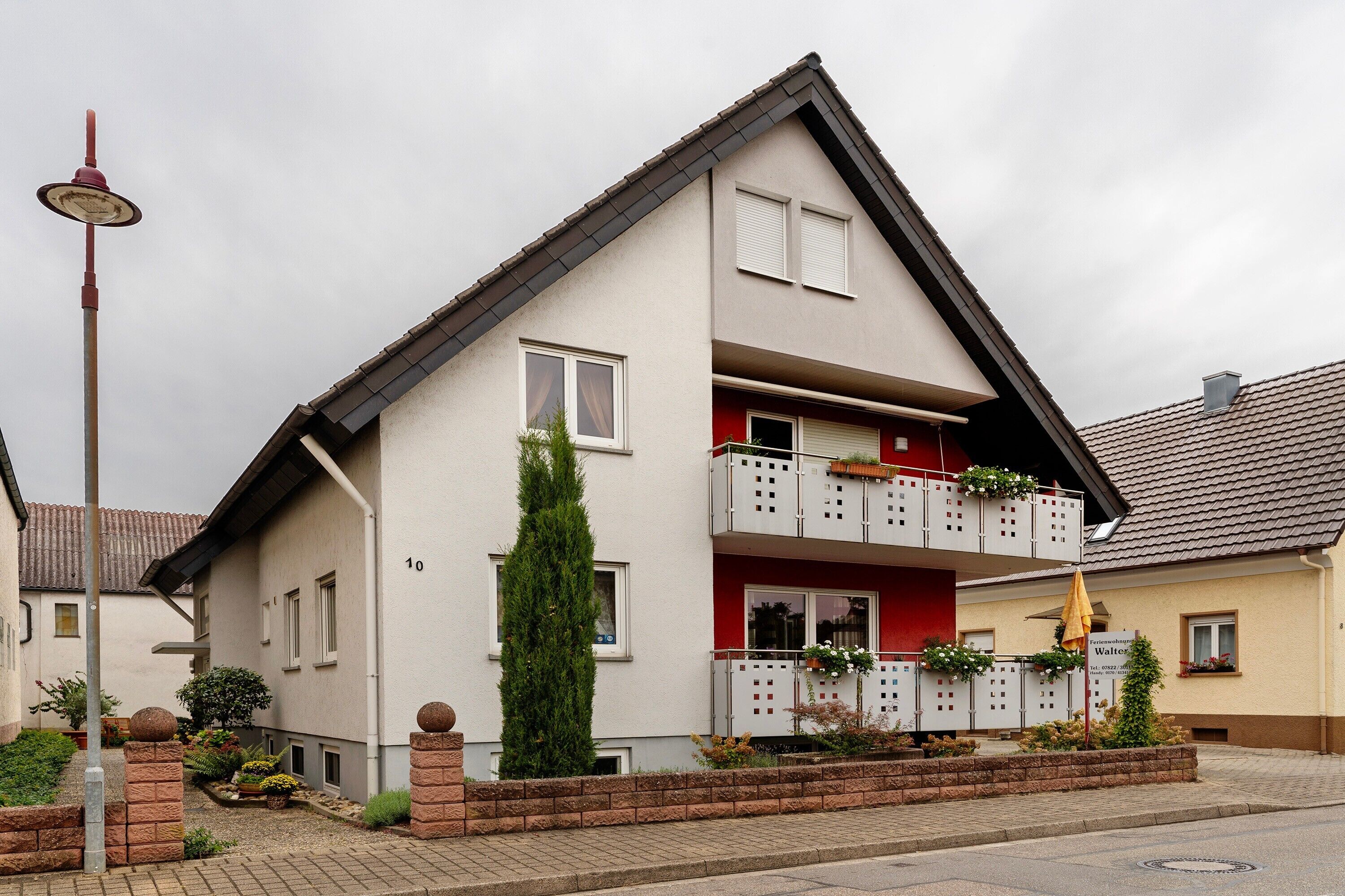 Ein zweistöckiges Wohnhaus mit Balkon, kleinem Garten und einer Straßenlaterne.