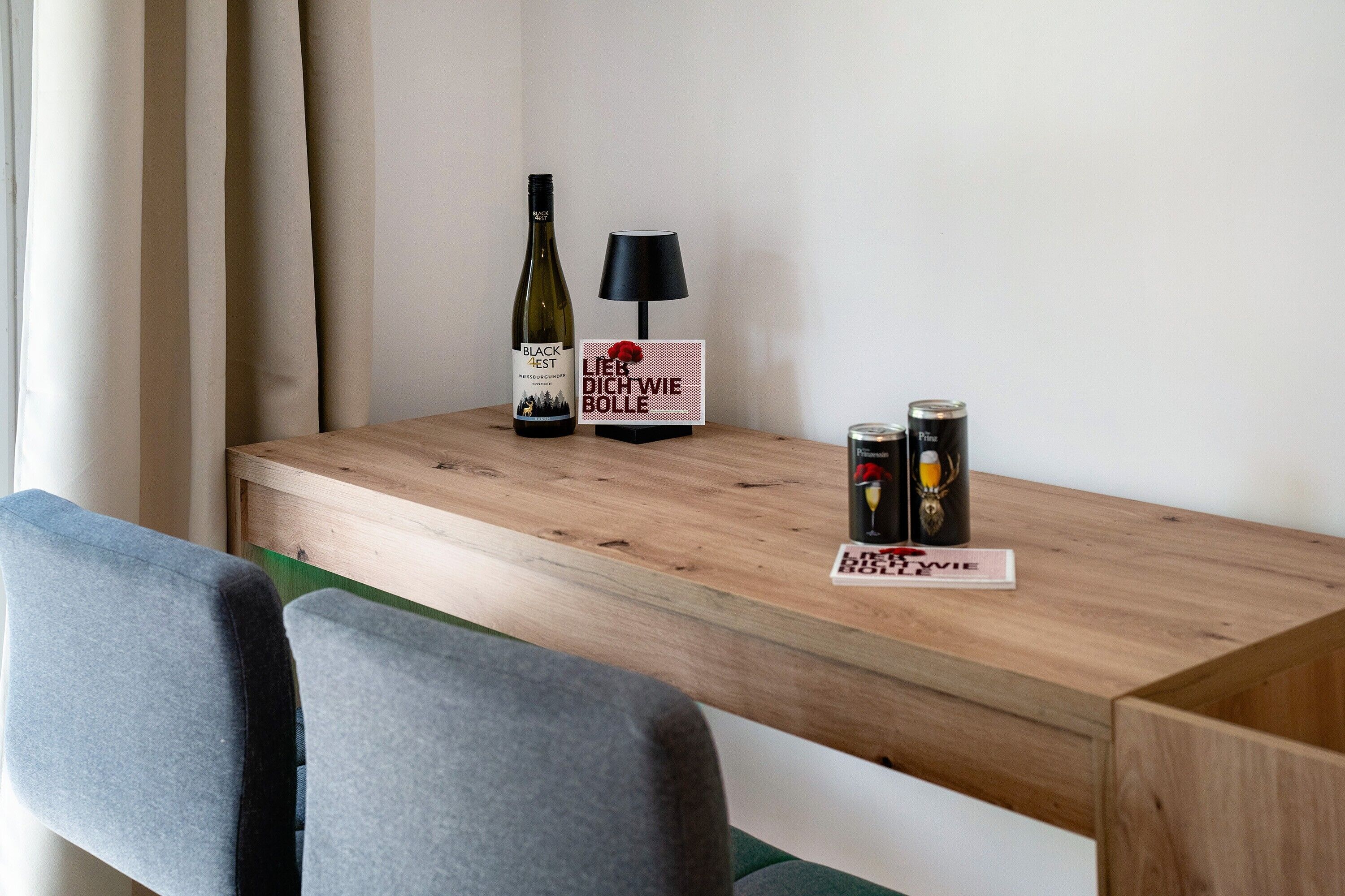 Une table en bois avec une bouteille de vin, une lampe et deux canettes.