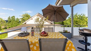 An outdoor patio with a table, chairs, a grill, and an umbrella.