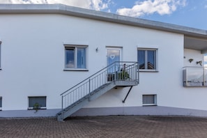 Un edificio moderno con fachada blanca, una escalera que lleva a un balcón y ventanas pequeñas.