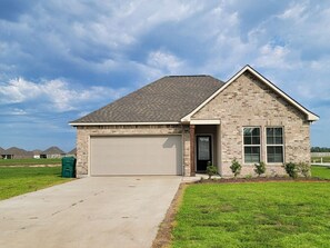 Une maison de plain-pied avec un garage, une porte d’entrée et un petit jardin devant la maison, avec de la pelouse et des arbustes.