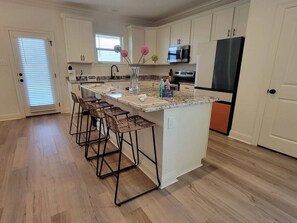Una cocina con una isla central, taburetes de bar, microondas y refrigerador.