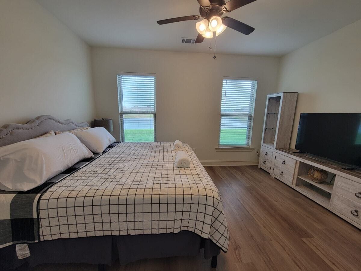 Ein Schlafzimmer mit einem Bett, einem Fernseher, einem Deckenventilator und zwei Fenstern.