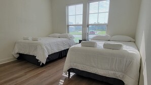 Habitación de hotel con dos camas, piso de madera y ventana con persianas.