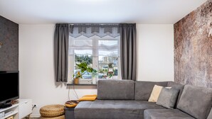 Un salon moderne avec un canapé gris, un téléviseur à écran plat et une grande fenêtre avec des rideaux.