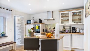 Une cuisine moderne avec des meubles blancs, un four encastré, un four à micro-ondes et une machine à café. On y trouve également un coin repas avec deux chaises et un banc.
