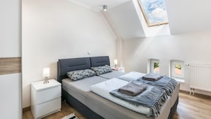 A bedroom with a skylight, a bed with pillows, a nightstand, and a radiator.