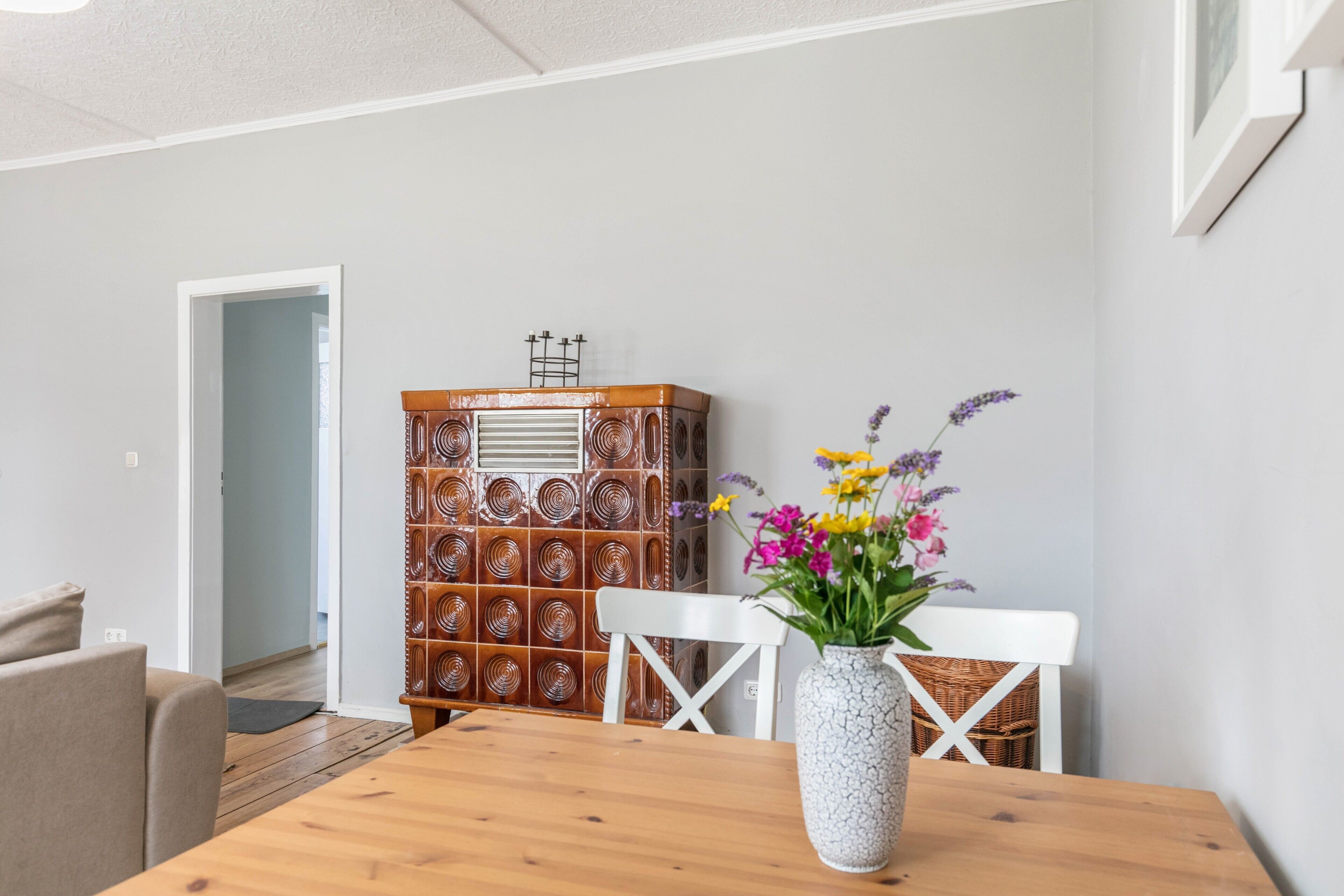 Un coin repas avec une table en bois, des chaises blanches, un vase de fleurs et un buffet à motifs.