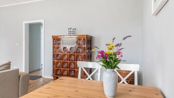 Un coin repas avec une table en bois, des chaises blanches, un vase de fleurs et un buffet à motifs.