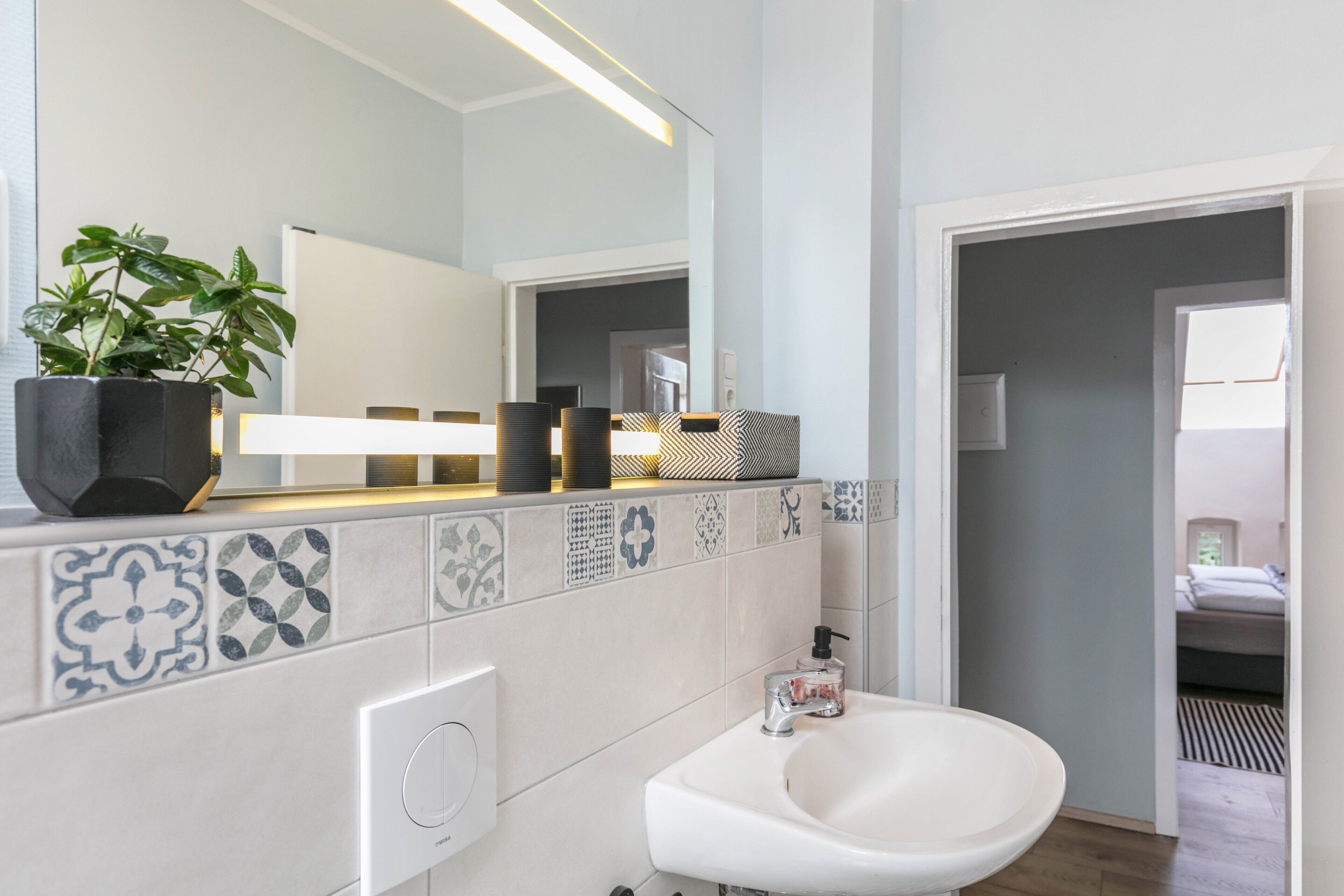 Un baño moderno con un lavabo blanco, un espejo y una planta en maceta.