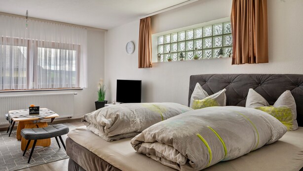 A bedroom with a bed, a TV, a window with curtains, a small table, and a chair.