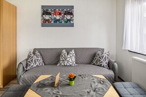 Un salon moderne avec un canapé gris, des coussins à motifs géométriques, une petite table sur laquelle est posé un vase de fleurs et une œuvre d’art accrochée au mur.