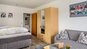 A bedroom with a bed, a wardrobe, a sofa, and a small table with a plant.