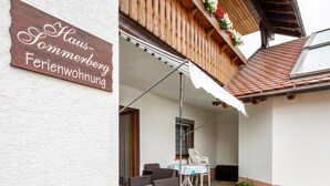 A wooden sign with text, a covered patio area with wicker furniture, and a green carpet.